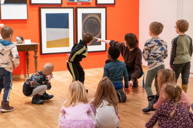 Formidling av billedkunst i utstillingen. Små barn og formidler sitter på gulvet og ser på kunsten.